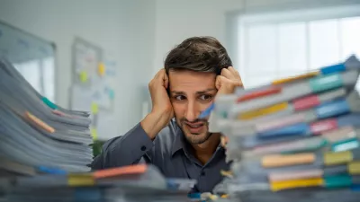 Tired Hispanic employee dealing with overwhelming workloads indoors, experiencing anxiety and pain from work-related challenges and deadlines.