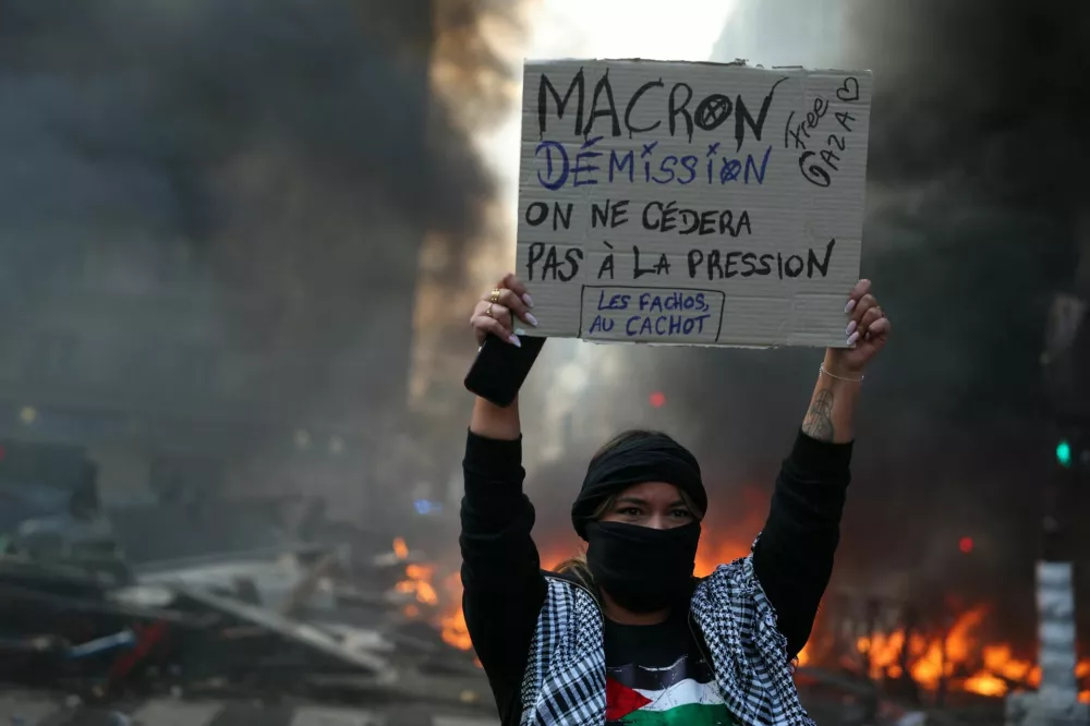 A masked protester holds a placard reading "Macron must resign, we will not yield to pressure" amid clashes during a day of demonstrations against the cost of living and rising fuel prices in Paris as part of nationwide protests called by the "Yellow Vests" movement, joined by French high school and university students, teachers and parents demanding better school conditions and government action, as well as labour unions, workers, farmers and retirees, France, October 17, 2026. REUTERS/Stephanie Lecocq&nbsp;