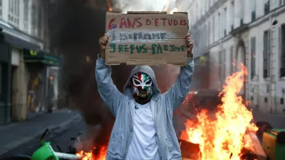 A person wearing a mask holds a placard reading "6 years of education, 1 diploma, 9 rejections a day" in front of burning flames, the day after a national day of demonstrations against the cost of living and rising fuel prices, in Paris, France, October 18, 2026. REUTERS/Abdul Saboor
