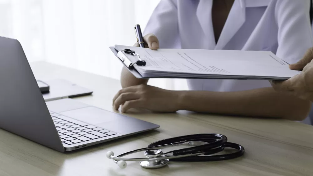 Doctor giving medical health report prescription and work on laptop computer at office desk in clinic or hospital.