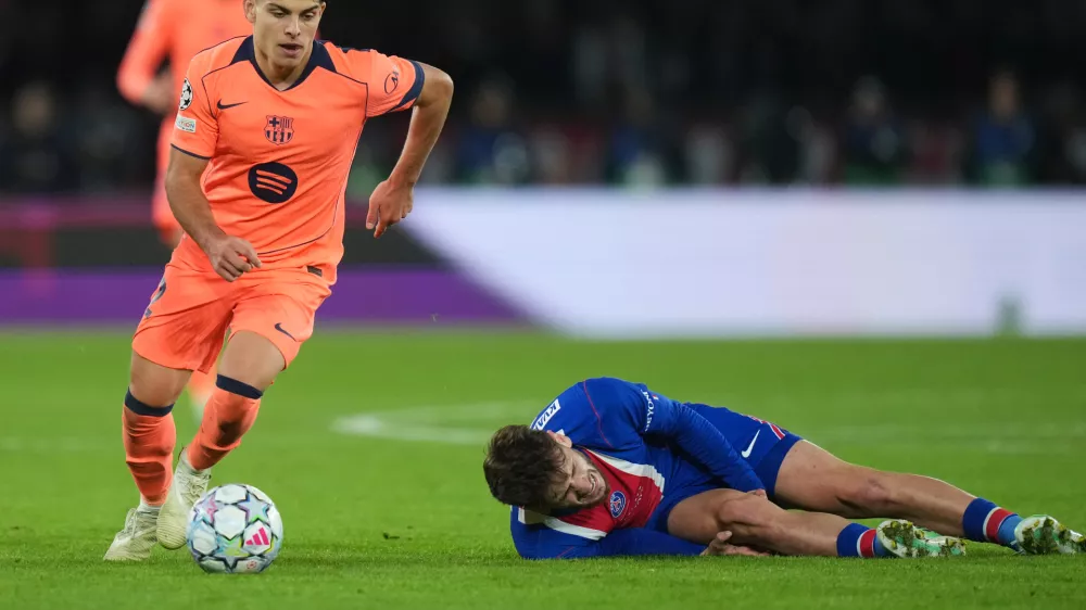 PSG's Khvicha Kvaratskhelia grimaces in pain after a challenges for the ball with Barcelona's Xavi Espart, left, during the Champions League opening phase soccer match between Paris Saint-Germain and FC Barcelona in Paris, Tuesday, Oct. 20, 2026. (AP Photo/Thibault Camus)