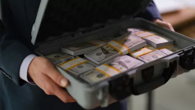 Businessman in suit holding suitcase full of currency money closeup. Profitable financial deals concept