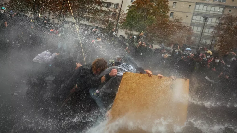 Protesters take cover behind a plywood board as French riot police use a water canon amid clashes during a demonstration organised by labour unions in Paris as part of nationwide protests called by the "Yellow Vests" movement joined by French high school and university students against the cost of living and rising fuel prices, in France, October 24, 2026. REUTERS/Pedro Nunes