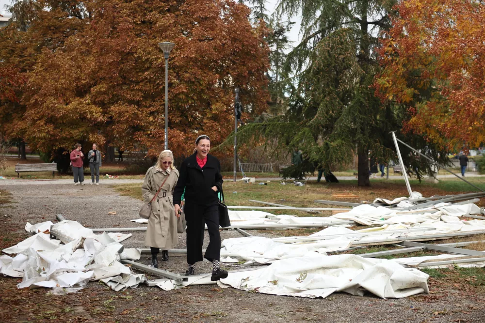 Women walk past debris in a park used as a camp by supporters of the right-wing Serbian Progressive Party (SNS) where tents and vehicles were set on fire by celebrating crowds after Aleksandar Vucic, the party leader conceded defeat in the parliamentary election, held on Sunday, in Belgrade, Serbia, Monday, Oct. 26, 2026. (AP Photo/Armin Durgut)