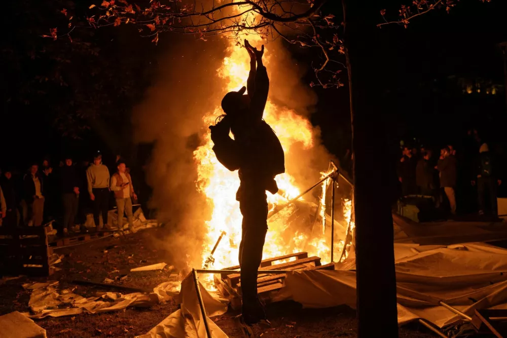 A person celebrates in front of a fire burning at Pionirski Park, site of a government-backed counter-encampment, as supporters of the electoral list "Student List - Students Win" celebrate after long-time ruler Aleksandar Vucic conceded defeat in the parliamentary election, in Belgrade, Serbia, October 25, 2026. REUTERS/Uros Arsic   TPX IMAGES OF THE DAY