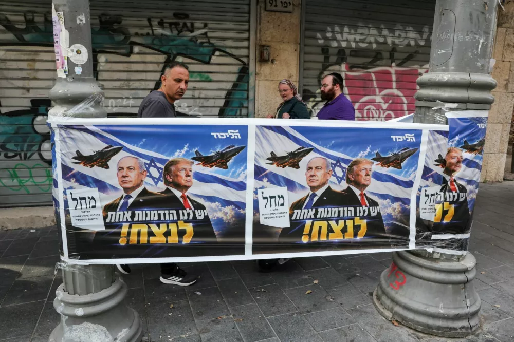 People walk past a poster of Israeli Prime Minister and Likud party leader Benjamin Netanyahu and US President Donald Trump during the country's national elections in central Jerusalem, October 27, 2026. REUTERS/Kevin Coombs    TPX IMAGES OF THE DAY