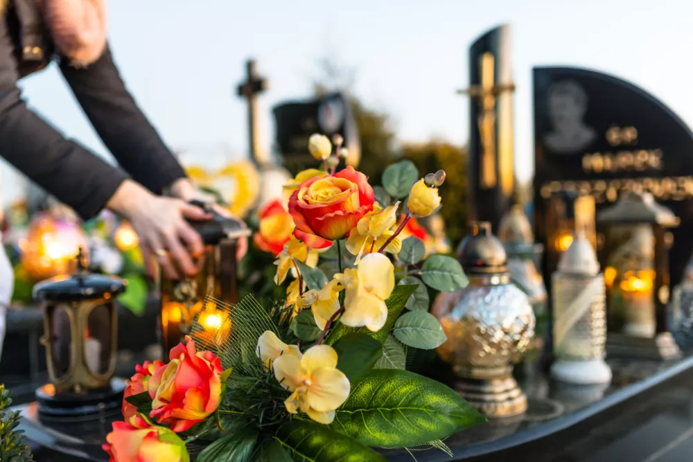 Artificial and real flowers and lit candles lying on the tombstone in the cemetery.
