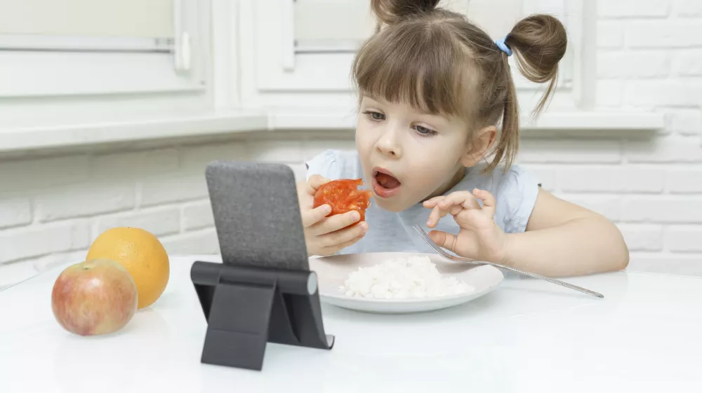 kid girl eating food and watching cartoons on a smartphone